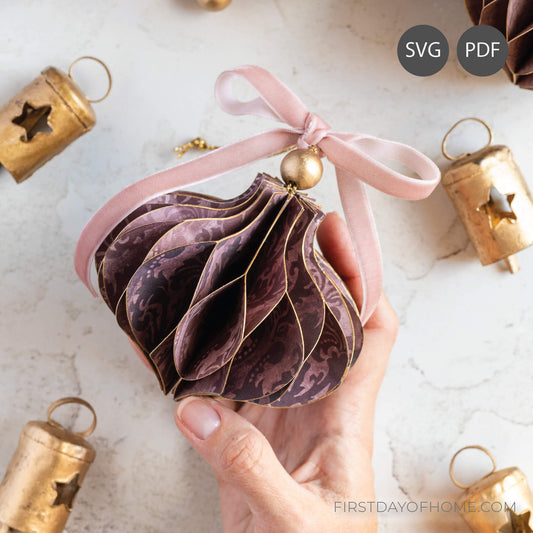 Hand holding a decorative honeycomb paper ornament with a pink ribbon against a light background.